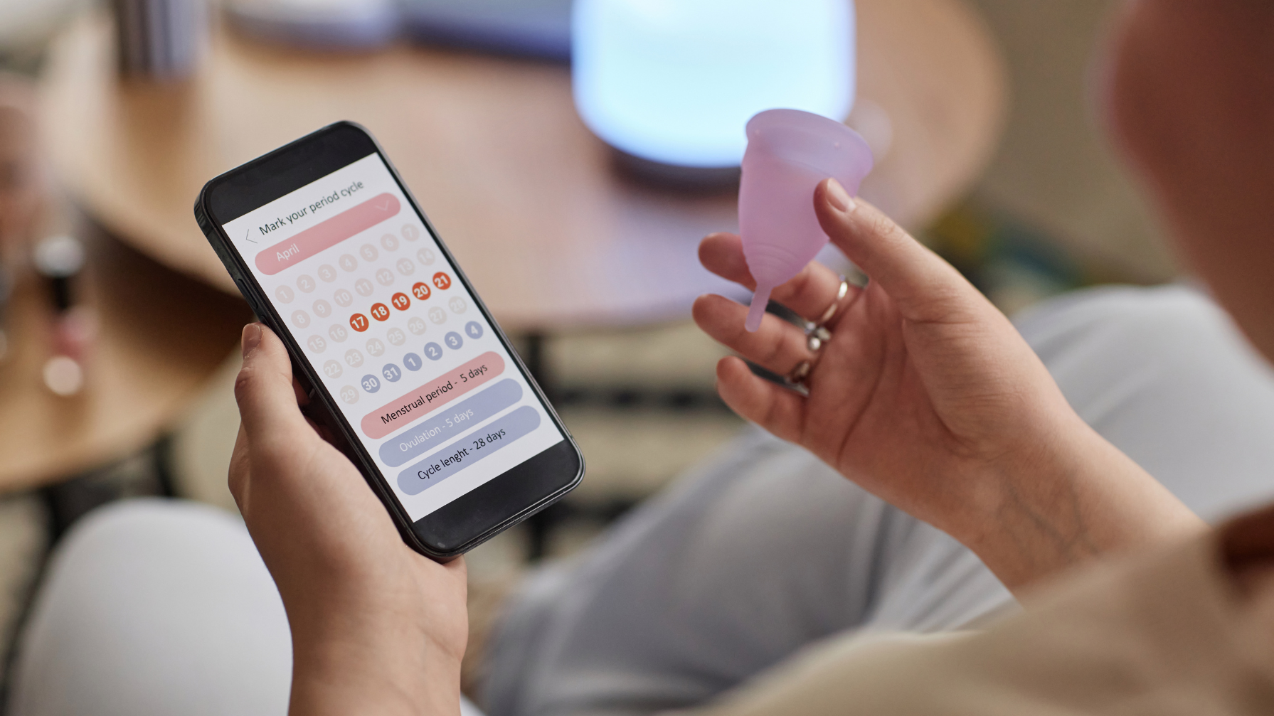 An image of someone holding a menstrual cup and consulting a generic period app
