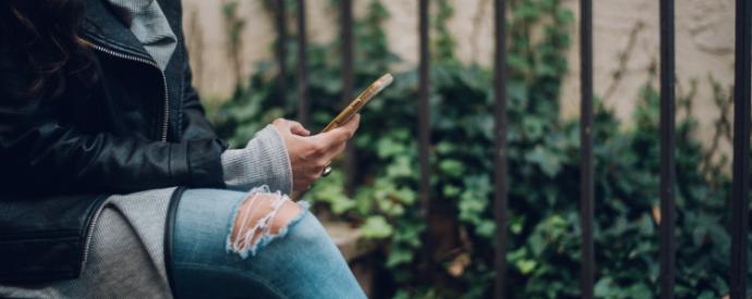 A woman sat on outside steps using a gold smartphone