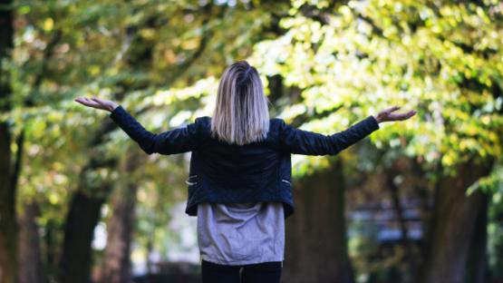The back of a woman shrugging facing trees in daylight
