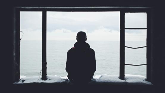 Man in silhouette sitting on a window ledge looking out to sea