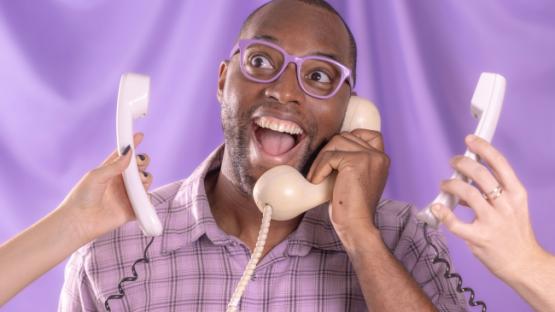 A man smiling holding a phone and surrounded by phones