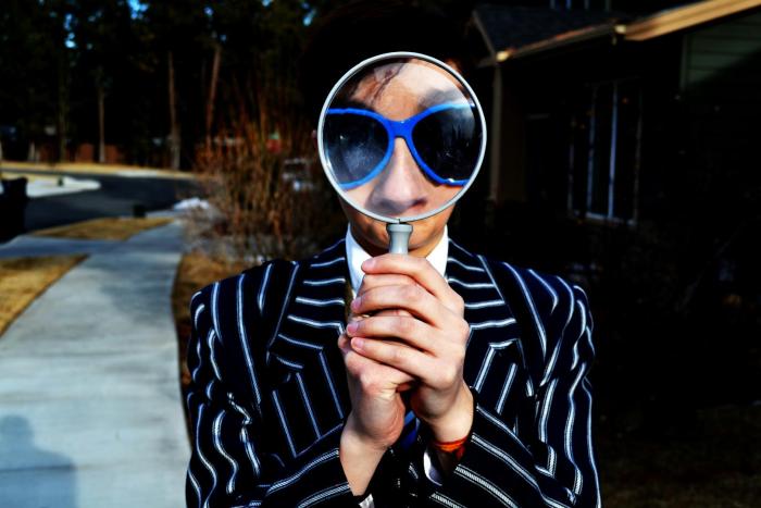 A person in sunglasses holding a magnifying glass in front of their face