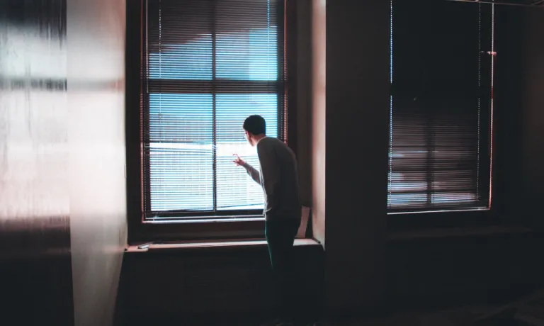 Man looking at the window behind curtains