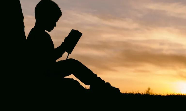 Silhouette of a child reading a book in front of a sunset
