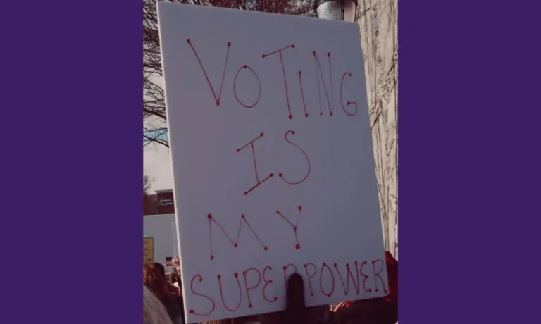 Protest placard with text: "VOTING IS MY SUPERPOWER" on purple background