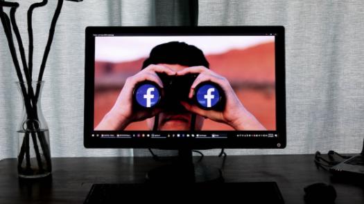 screen with individual holding binoculars with facebook sign on end