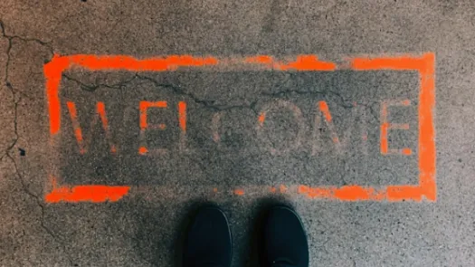 Feet standing in front of faded orange 'welcome' message on ground