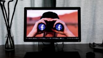 screen with individual holding binoculars with facebook sign on end