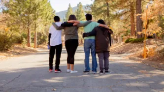 Four friends looking down a road with their arms around each other.