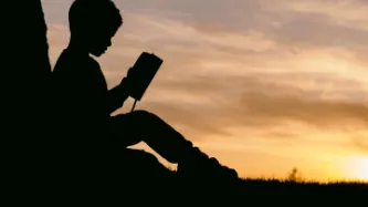 Silhouette of a child reading a book in front of a sunset