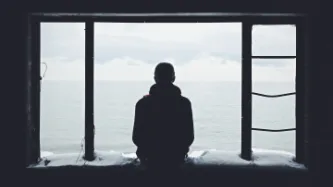 Man in silhouette sitting on a window ledge looking out to sea