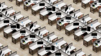 Uniform grid of endless rows of desk cubicles with laptops and monitors